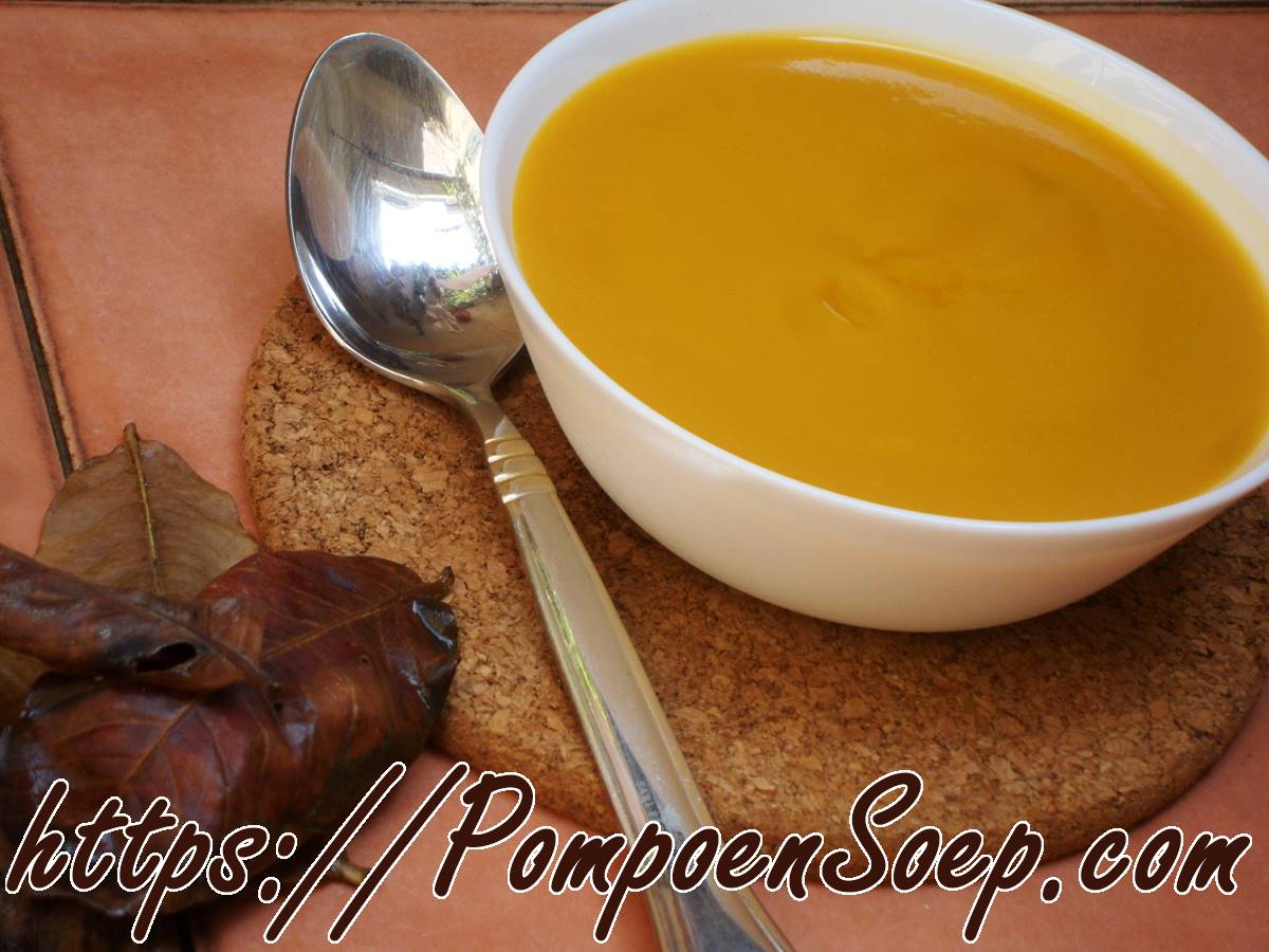 Kom romige pompoensoep zonder room, glad gepureerd en mooi oranje, geserveerd met lepel naast herfstbladeren.