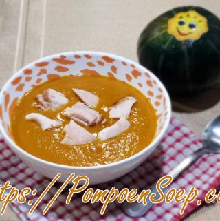 Kom pompoensoep met kip geserveerd op rood-wit servet, met klein pompoentje ernaast