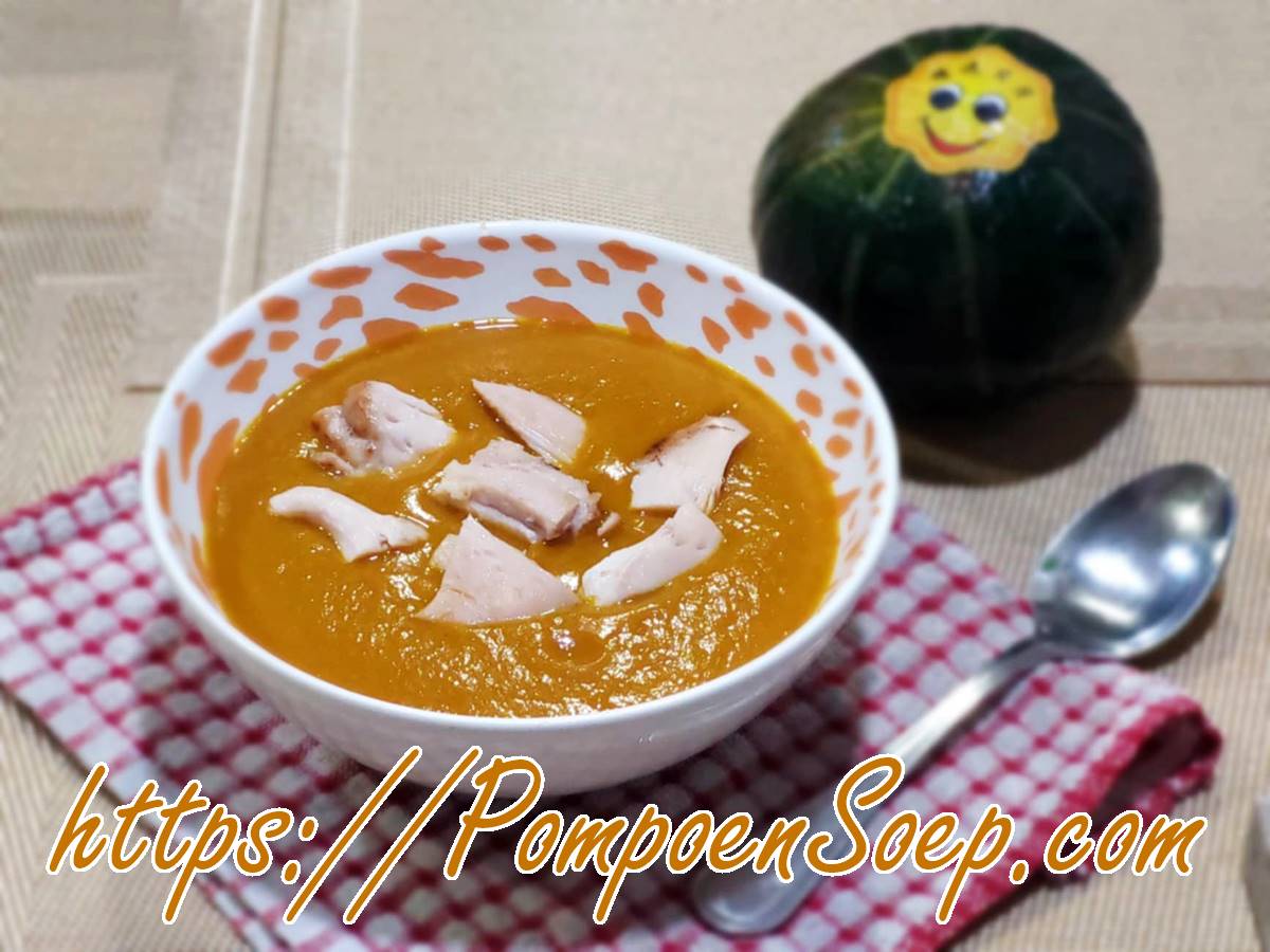 Kom pompoensoep met kip geserveerd op rood-wit servet, met klein pompoentje ernaast