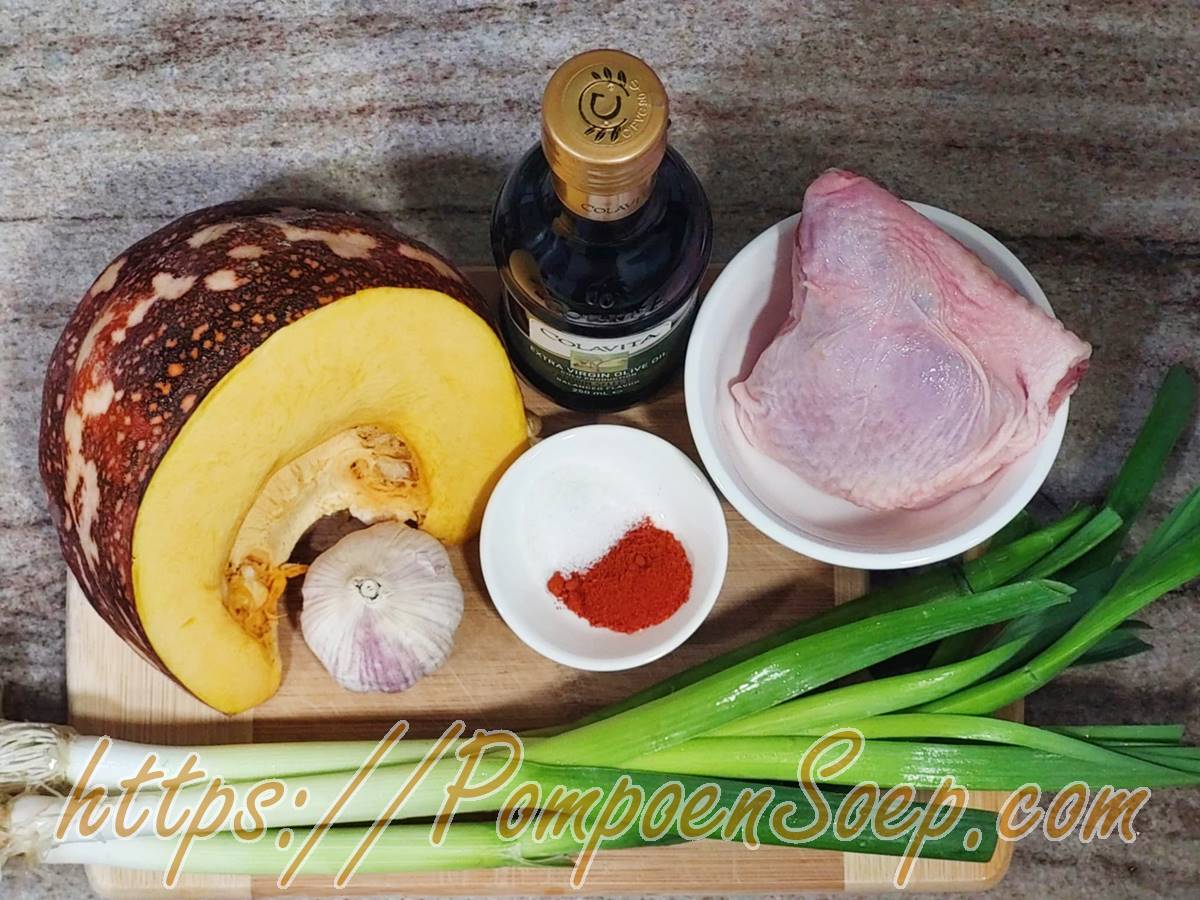 Pompoen, kip, prei, ui, knoflook, paprikapoeder en olijfolie op een houten plank voor pompoensoep met kip.